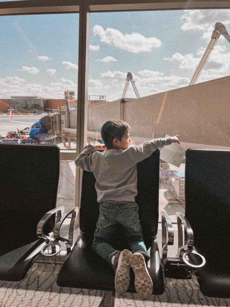 young boy in airport pointing in front of a window with airplane in the background tsa precheck for kids